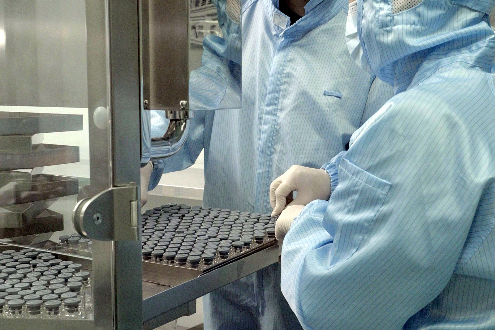 Operators in full cleanroom suits loading trays of stoppered vials on the filling line